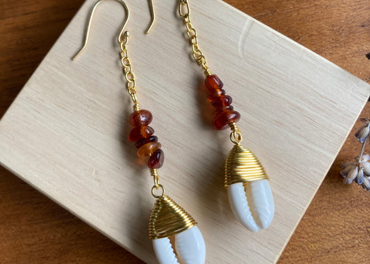 Hessonite Garnet and cowrie gold coloured copper wire findings, dangle drop earrings, displayed on wooden block with lavender flowers slightly in frame